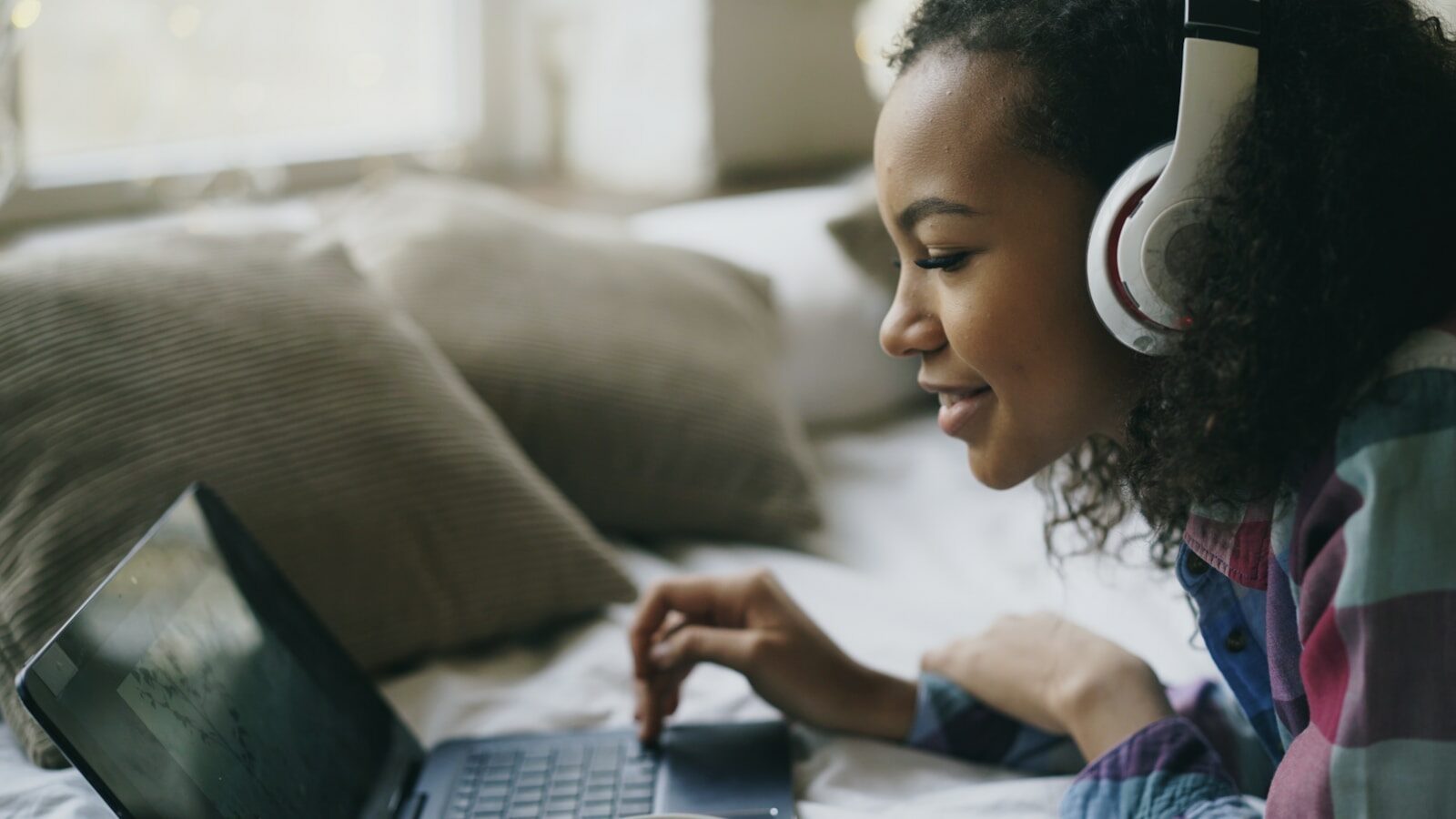 Young woman with headphones using laptop on bed.